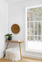 Tabouret blanc moelleux et petite table en bois à côté de la fenêtre