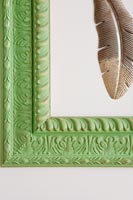 Cadre photo en bois peint en vert sur mur avec plume sculptée