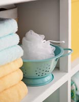 Passoire miniature avec chiffon exfoliant et serviettes sur l'étagère de la salle de bain