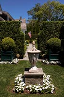 Lanterne dans un jardin à la française avec vue à travers une haie sur le drapeau américain sur la maison