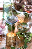 Verres colorés et bougie sur table à manger avec feuillage décoratif