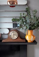 Tiges de feuillage dans une cruche en céramique et horloge vintage sur cheminée