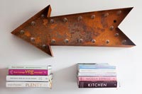Oeuvre légère en forme de flèche en métal rouillé et livres sur des étagères flottantes