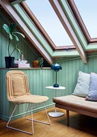 Chaise dans un coin de la pièce avec de grandes fenêtres de toit et des murs en bois peint