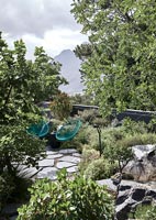 Chaises de jardin vertes sur une petite zone pavée de jardin avec vue panoramique sur la montagne