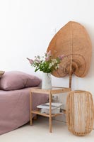 Ventilateur en sisal derrière une table de chevet en bois dans une chambre de campagne