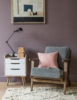 Mur peint en violet derrière le fauteuil et l'armoire