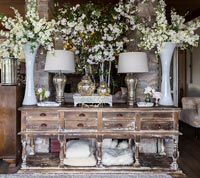 Fleurs blanches affichées dans de grands vases sur un buffet en bois vieilli
