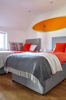 Planche de surf orange vif au-dessus de lits jumeaux dans une chambre moderne