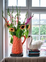 Vase cruche orange vif plein de fleurs sur le rebord de la fenêtre