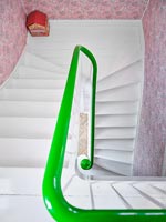 Vue vers le bas de l'escalier blanc avec rampe peinte en vert et papier peint rose