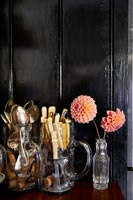 Couverts dans des cruches en verre à côté de dahlias dans un vase contre le mur noir