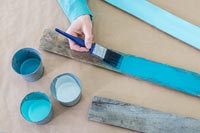 Femme peint une planche en bois rustique dans différents tons de turquoise à l'aide d'un pinceau