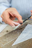 Close up detail of woman using a paint brush to flick paint on wood to simulate snow Falling