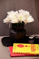 Vase noir avec des fleurs coupées blanches sur la table de chevet avec du matériel de lecture