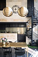 Salle à manger or et noir avec vue sur cuisine moderne et escalier en colimaçon en fer forgé noir