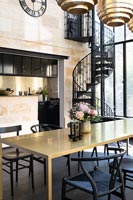 Salle à manger moderne noir et or avec vue sur cuisine et escalier en colimaçon en fer forgé