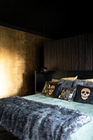 Chambre noire et or avec jet de fourrure et coussins à motifs de crâne sur le lit