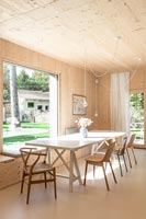 Salle à manger moderne dans une maison en bois avec grande baie vitrée avec vue sur jardin