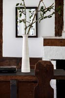 Vase long blanc avec des branches d'arbres comme arrangement dans la salle à manger du pays