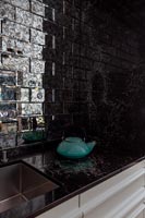 Bouilloire turquoise sur plan de travail de cuisine noir avec carrelage brillant derrière