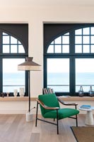 Fauteuil vert et lampadaire vintage à côté de grandes fenêtres avec vue sur la mer