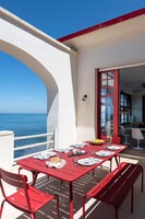 Table à manger extérieure dressée pour le déjeuner sur une terrasse rouge et blanche avec vue sur la mer