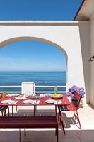 Table à manger rouge dressée pour le déjeuner sur la terrasse avec vue sur la mer