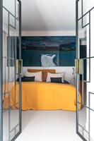 Vue à travers les portes intérieures en verre ouvertes à la chambre moderne avec de grandes œuvres d'art au-dessus du lit