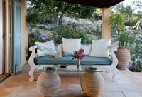 Canapé en bois orné sur terrasse couverte avec table en verre et urne en argile