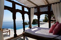 Pergola décorative avec grand lit sur terrasse extérieure avec piscine et vue mer
