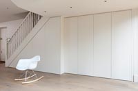 Couloir blanc minimal avec placards sous escalier intégrés et chaise simple