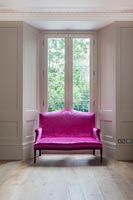 Canapé rose vif à côté de la fenêtre dans le salon lambrissé
