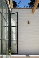Porte en verre à cadre noir à la terrasse contre le mur extérieur peint en blanc