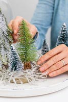 Femme ajoutant de faux arbres de Noël miniatures au bac