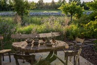 Table et chaises rustiques sur terrasse donnant sur jardin de campagne en été