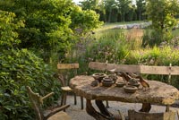 Table et chaises rustiques sur terrasse donnant sur jardin de campagne en été