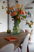 Arrangement de fleurs coupées rouge et orange dans un vase sur table à manger