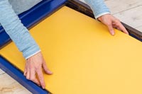 Femme plaçant un panneau de liège recouvert de tissu dans un cadre nouvellement peint