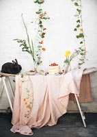 Lapin de compagnie sur table de jardin remplie de fleurs et de nourriture de pique-nique
