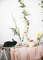 Lapin de compagnie sur table de jardin remplie de fleurs et de nourriture de pique-nique