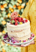 Femme tenant un gâteau de célébration couvert de fruits et de fleurs