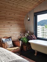 Fauteuil en cuir vintage et baignoire dans une chambre en bois moderne