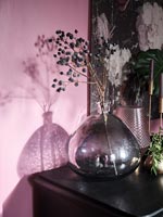 Vase en verre noir avec têtes de graines contre mur peint en rose