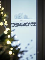 Vue sur la campagne couverte de neige à travers la fenêtre à côté de l'arbre de Noël