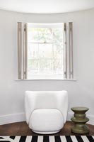Chaise blanche moderne à côté de la fenêtre avec volets ouverts