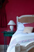 Tête de lit en rotin contre mur peint en rouge dans la chambre à coucher du pays