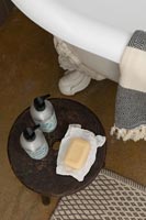 Savon et articles de toilette sur une petite table en bois à côté de la baignoire