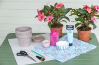 Tissu, pots en terre cuite, soucoupes en terre cuite, peinture acrylique, colle, ciseaux, pinceau, crayon, papier et fleurs disposés sur une table