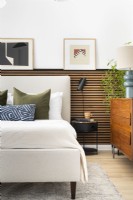 Chambre classique moderne avec lit rembourré crème avec tête de lit, mur à lattes, applique murale et étagère à photos.